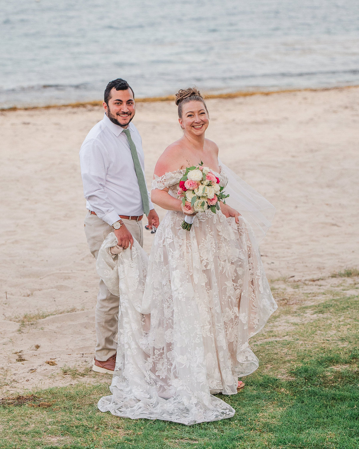 Couple standing on a beach with the woman holding a bouquet.