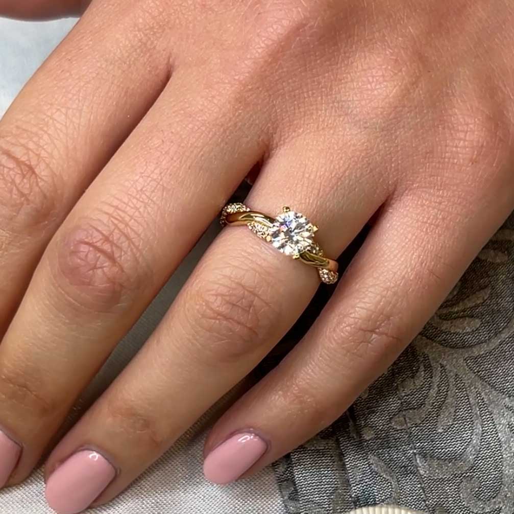 Shown in 1.0 Carat Diamond*The Amelia Twist Engagement Ring with round cut Moissanite in yellow gold on model hand by Lisa Robin#color_14k-yellow-gold
