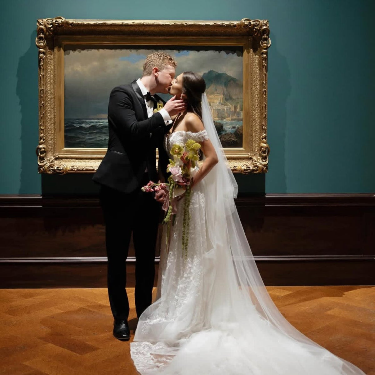 Couple in wedding attire kissing in front of a painting at the Dayton Art Institute