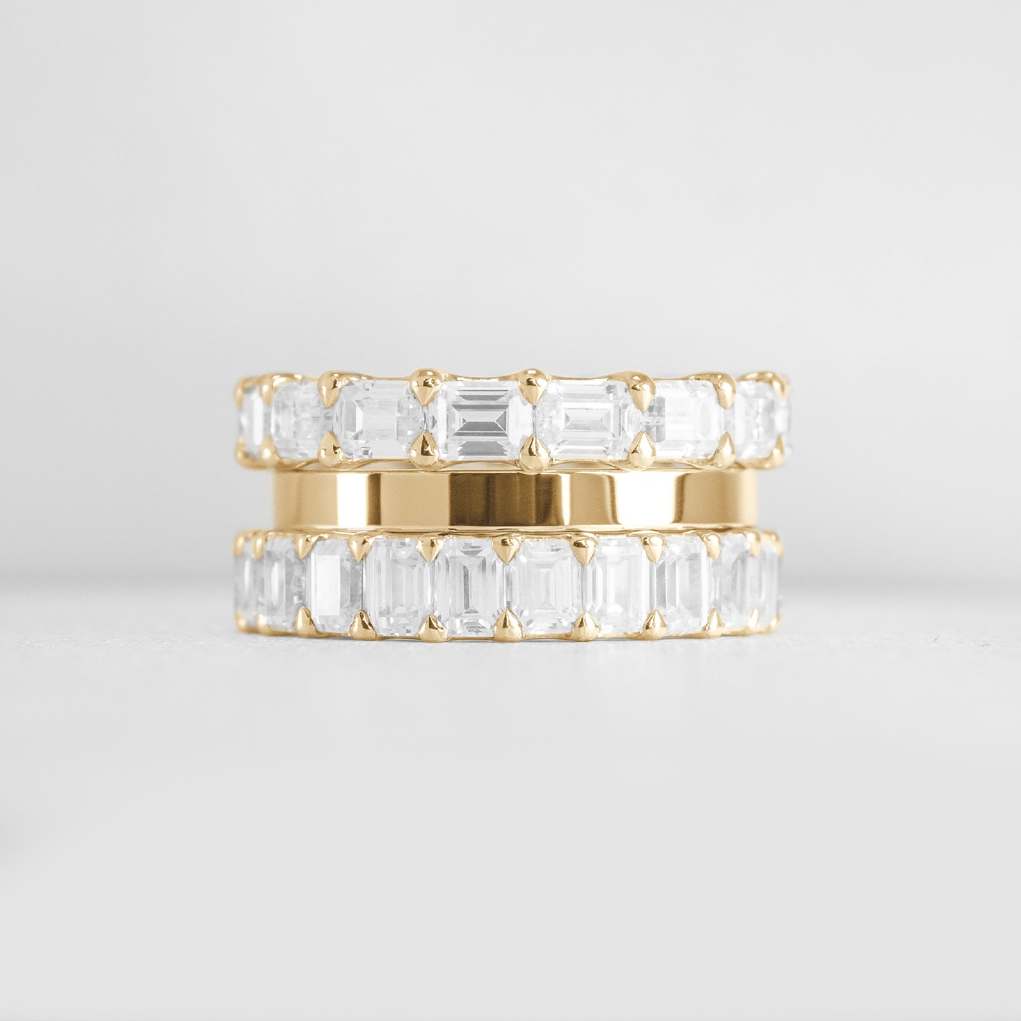 The Ensemble Ring Stack Set comprised of the Avery East West Emerald Cut Eternity Diamond Wedding Ring in 14K yellow gold with Jamie 2mm Wide Flat Wedding Ring in 14K yellow gold and Aniston Emerald Cut Diamond Eternity Wedding Ring in 14K yellow gold from front by Lisa Robin#color_14k-yellow-gold