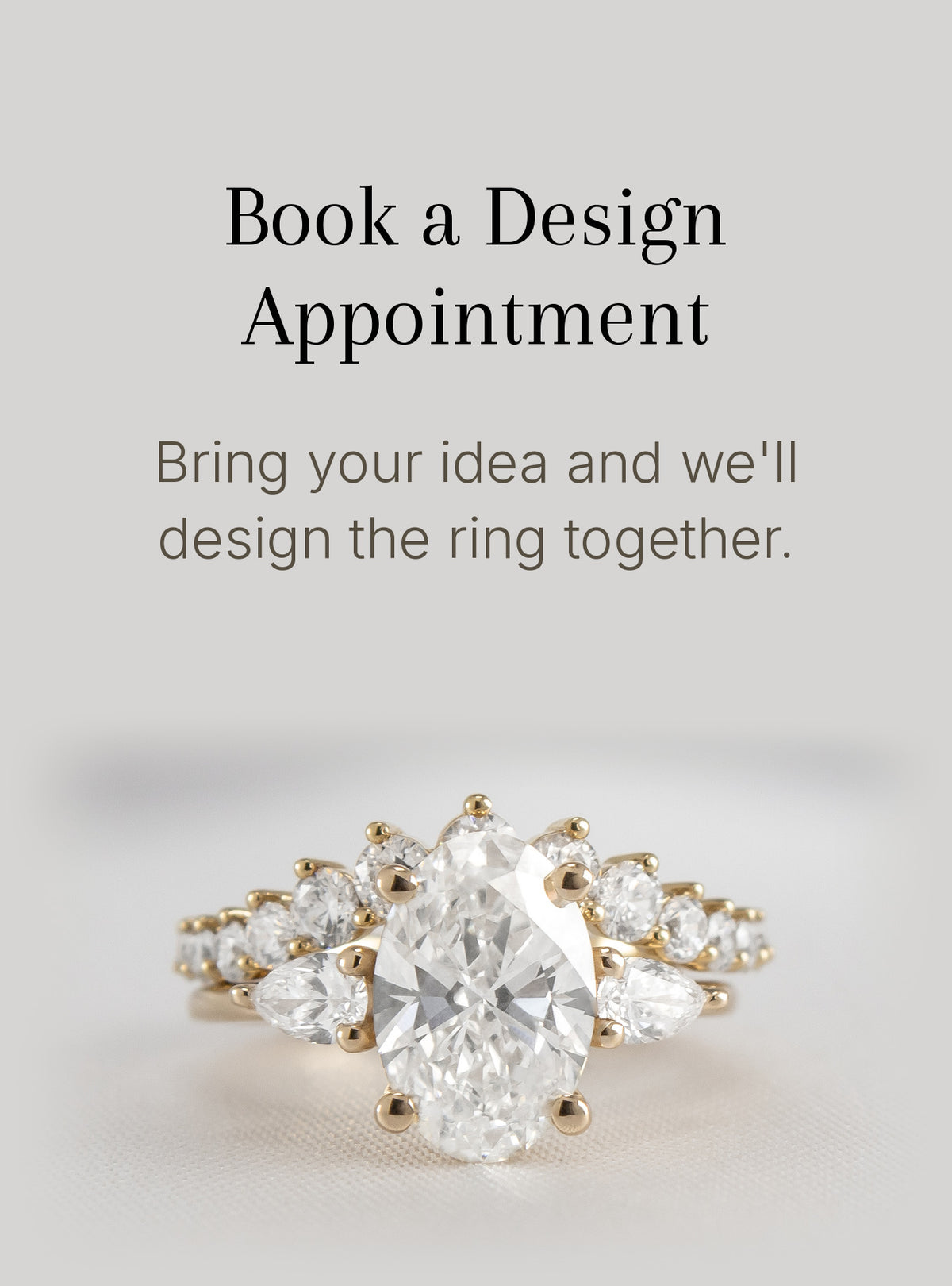 A gold ring with a large oval clear center stone and smaller clear stones along the band, shown on a light gray background with text that reads 'Book a Design Appointment' and 'Bring your idea and we'll design the ring together.'.