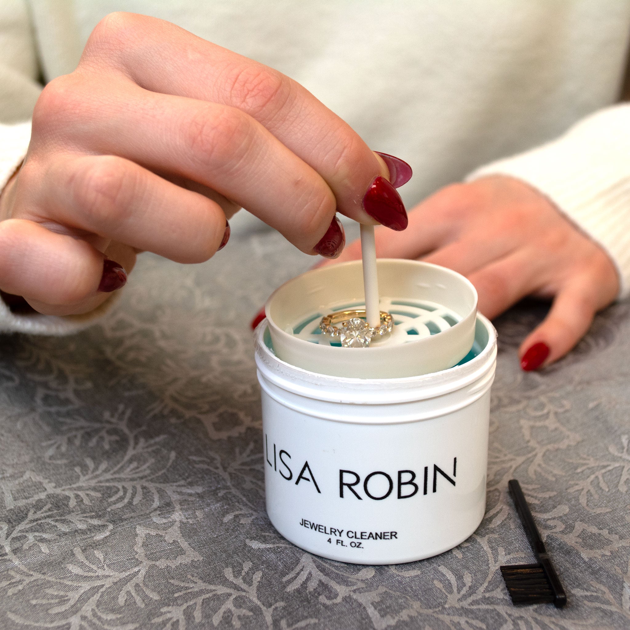 Person using a jewelry cleaner with 'Lisa Robin' branding on a textured surface.